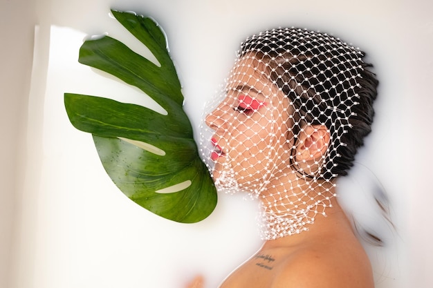 Foto justo por encima de la foto de una mujer joven con la cara cubierta por una red tomando un baño de leche