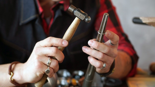 Juwelier in der Hand hält einen Hammer zum Herstellen von Schmuck. Nahansicht