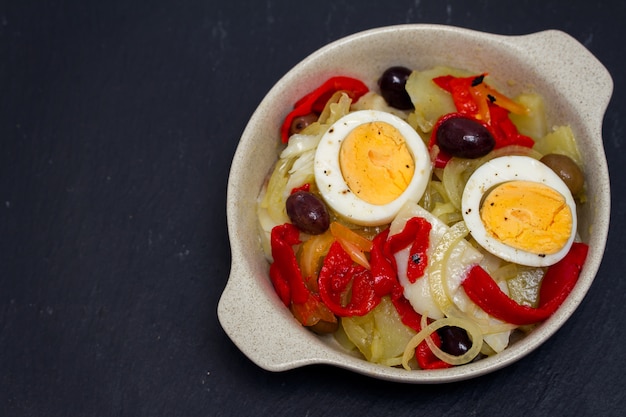 Kabeljau mit Kartoffeln, rotem Pfeffer, Ei und Oliven auf Teller