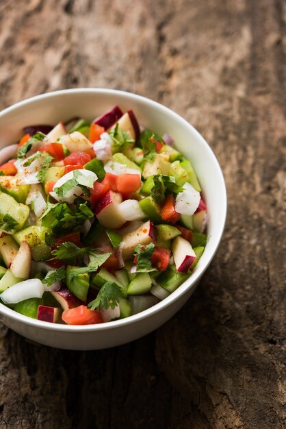 Kachumber OU Salada Verde Indiana, também conhecida como Koshimbir. Servido em uma tigela sobre um fundo mal-humorado. Foco seletivo