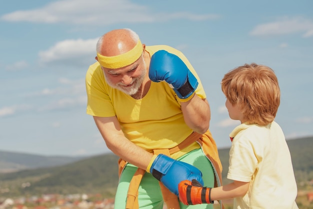 Kämpfer Boxer Großvater und Kind mit blauen Boxhandschuh auf Hintergrund des blauen Himmels isoliert Boxen Älterer junger Mann Boxen