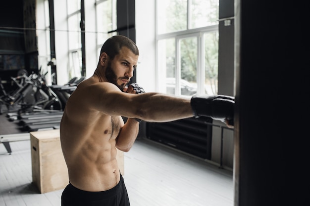 Kämpfer, der einige Tritte mit Boxsack übt Kick-Boxsack auf dunklem Hintergrund schwarzer Boxsack wiegt im Fitnessstudio hochwertige K-Aufnahmen