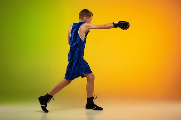 Kämpfer. Professionelles Boxertraining im Teenageralter in Aktion, Bewegung einzeln auf Farbverlaufshintergrund im Neonlicht. Treten, Boxen. Konzept von Sport, Bewegung, Energie und dynamischem, gesundem Lebensstil.