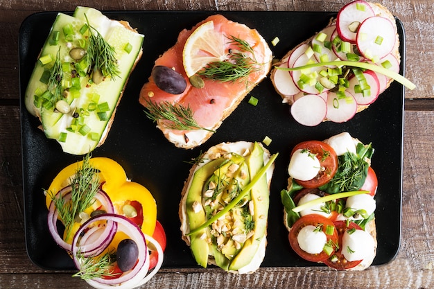 Käse, Gemüse und Lachse der Sandwiche oder der Tapas mit Sahne, über Weißbuchhintergrund.