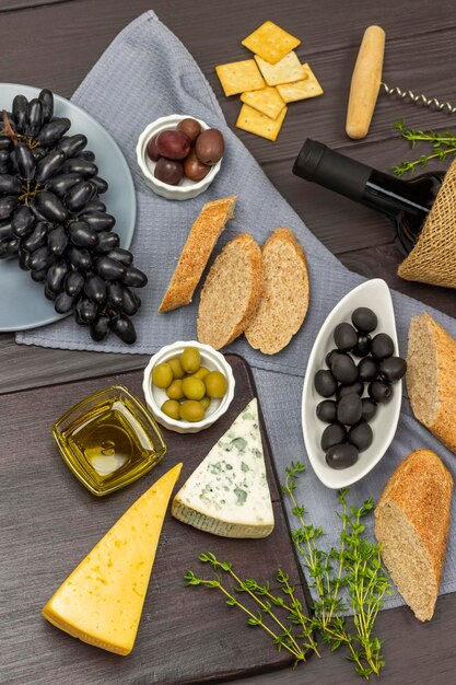 Käse, Olivenöl und Oliven auf einer Tafel Schwarze Oliven, ein Bündel schwarze Trauben und ein in Scheiben geschnittenes Baguette auf einer grauen Serviette