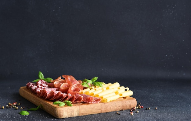 Foto käse-prosciutto-salami auf einem quadratischen holzbrett auf schwarzem steinhintergrund delikatesse