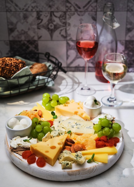 Käse-Set. Käseplatte mit Obst und einem Glas Weiß- und Rotwein auf weißem Hintergrund. Verschiedene Käsesorten auf einem Holzbrett.