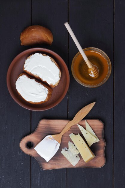 Käse und Sandwiches mit Weichkäse auf schwarzem Holzbrett Hartkäse und Sahne mit Holzbesteck Milchprodukte und Honig auf dunklem Hintergrund Draufsicht