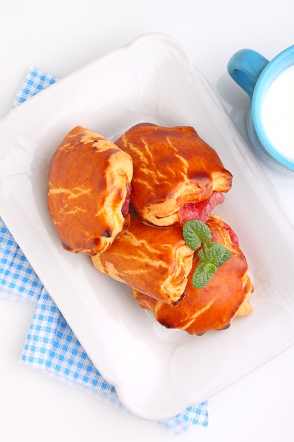 Käsebrötchen mit Kirschmarmelade. Blaue Tasse mit Milch. Weißer Hintergrund.