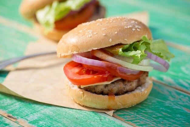 Käseburger mit gegrilltem Fleisch, Käse, Tomate, auf Kraftpapier auf Holzoberfläche.