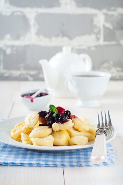 Käseknödel, Gnocchi mit Sauce aus schwarzen Johannisbeeren in einer weißen Keramikplatte für ein gesundes Frühstück