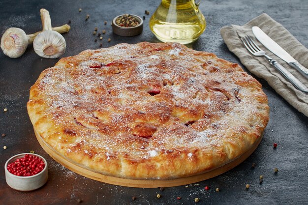 Käsekuchen auf runder Holzplatte mit Zutaten auf dunkler Oberfläche