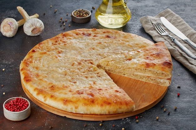 Käsekuchen auf runder Holzplatte mit Zutaten auf dunkler Oberfläche