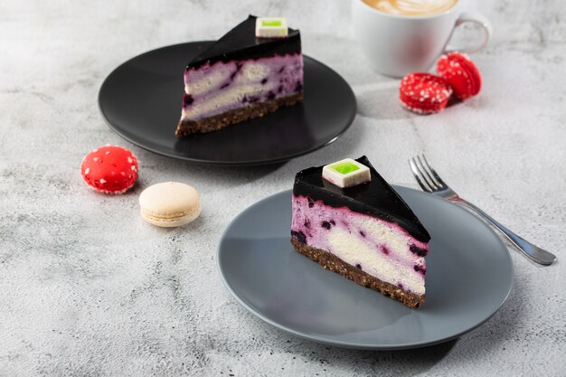 Käsekuchen mit Blaubeere mit Tasse Kaffee auf weißem Tisch. Nahaufnahme. Leckeres Frühstück. Stück Kuchen auf schwarzem Teller, weiße Tasse auf weißem Marmorhintergrund. Horizontales Foto.