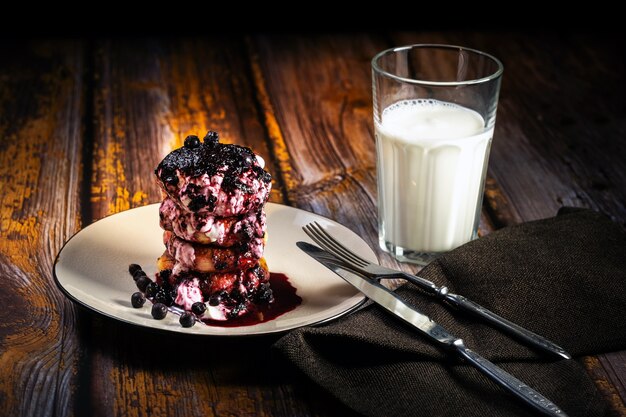 Käsekuchen mit Blaubeermarmelade und Sauerrahm auf einem Teller mit einem Glas Milch auf dem Tisch