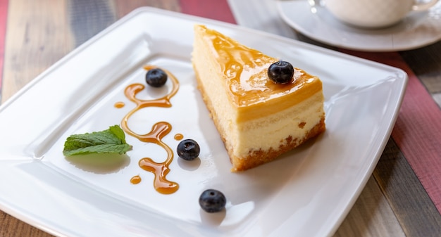 Käsekuchen mit Blaubeersoße auf weißer Platte und Tasse Kaffee auf Holztisch