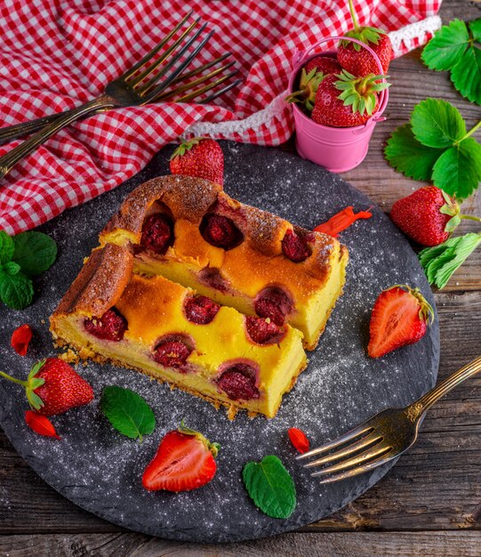 Käsekuchen mit Erdbeeren auf einer schwarzen Graphitplatte