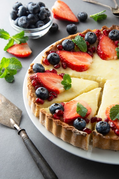 Käsekuchen mit frischen Beeren und Minze zum Nachtisch. Grauer Hintergrund.