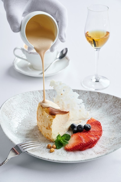 Käsekuchen mit frischen Erdbeeren und Blaubeeren auf weißem Teller und der Kaffee Latte stehen auf dem Tisch im Café und einem Glas Cognac