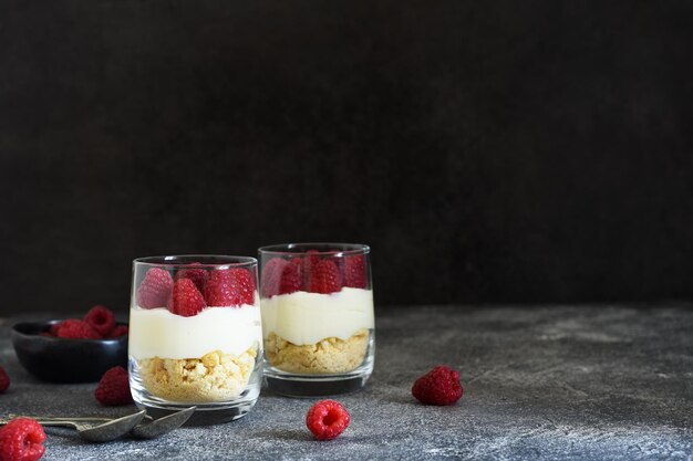 Käsekuchen mit Himbeeren in einem Glas auf Betonhintergrund Klassisches Dessert