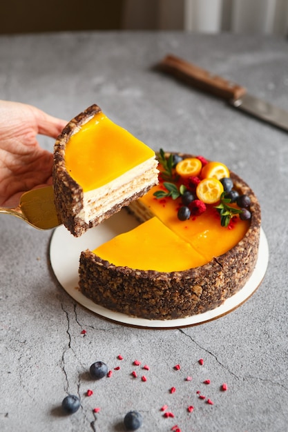 Käsekuchen mit Mangofrucht an einer grauen Wand, dekoriert mit Beeren und Früchten