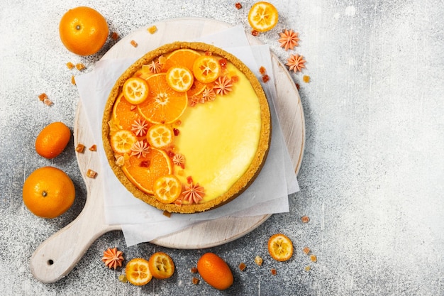 Foto käsekuchen mit orangen- und kumquatscheiben auf grauem steinhintergrund draufsicht