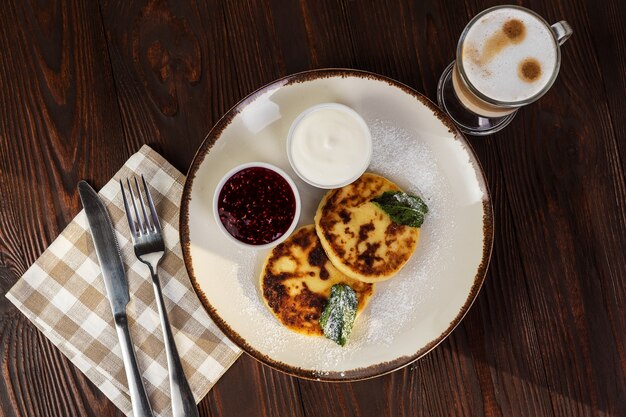 Käsekuchen mit Sauerrahmmarmelade und Kaffee Latte auf rustikalem Hintergrund. Flach legen