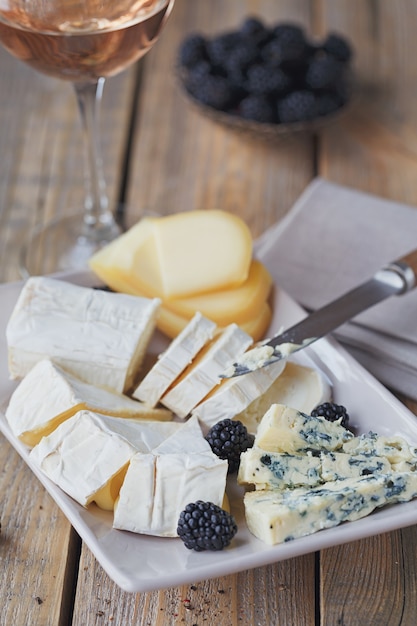 Käseplatte. Auswahl an Käse mit Beeren und einem Glas Roséwein auf Holzhintergrund.