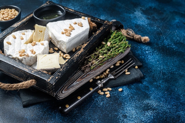 Käseplatte mit Brie und Camembert, Holztablett mit Nüssen. Französische Milchprodukte. Blauer Hintergrund. Ansicht von oben. Platz kopieren.