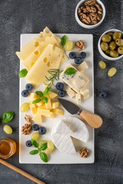 Käseplatte mit verschiedenen Käsesorten Honig Trauben Nüsse Oliven Heidelbeeren und frischen Kräutern