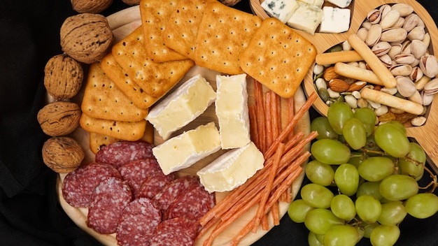 Käseplatte mit verschiedenen Käsetrauben Nüssen auf schwarzem Hintergrund