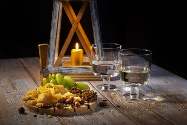 Käseplatte mit verschiedenen Snacks auf dem Tisch mit zwei Gläsern Wein bei Kerzenschein