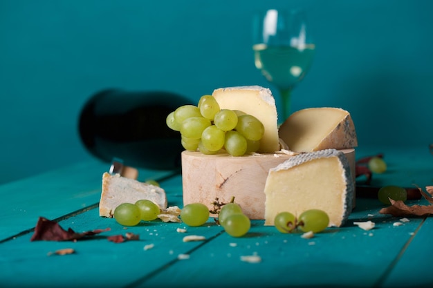 Käsescheiben, weiße Trauben, Messer, Glas und eine Flasche Weißwein auf einer Holzoberfläche. Nahaufnahme