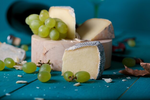 Käsescheiben, weiße Trauben, Messer, Glas und eine Flasche Weißwein auf einer Holzoberfläche. Nahaufnahme