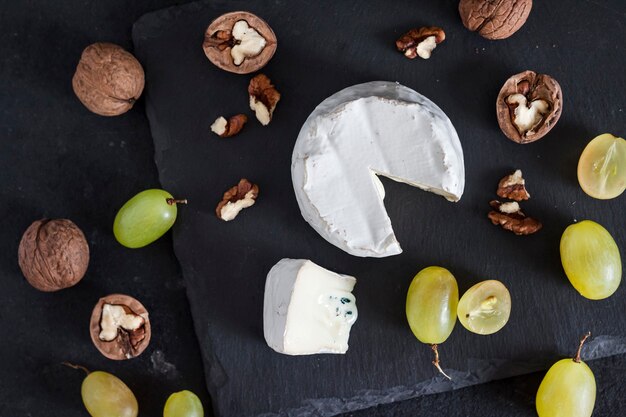 Käsesorte Brie. Weichkäse mit Trauben und Walnüssen auf schwarzem Hintergrund. Flache Lage, Ansicht von oben