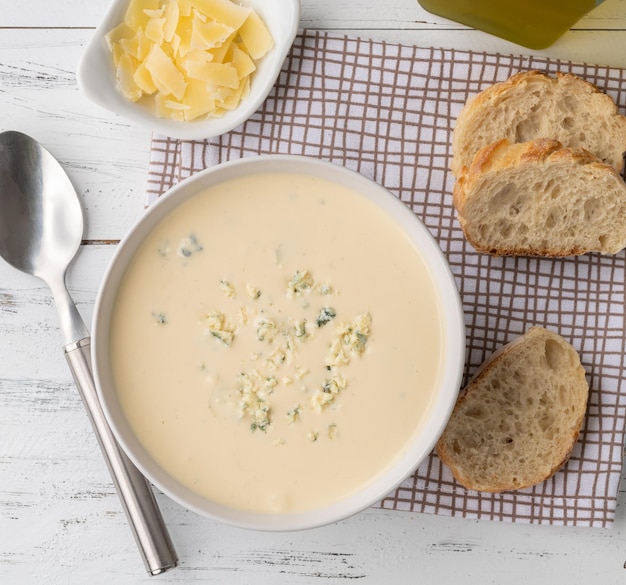 Käsesuppe in einer Schüssel mit Brotscheiben und Gewürzen über Holztisch