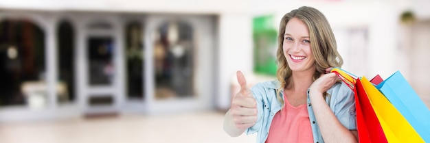 Foto käufer mit taschen, die daumen gegen ein verschwommenes einkaufszentrum aufgeben