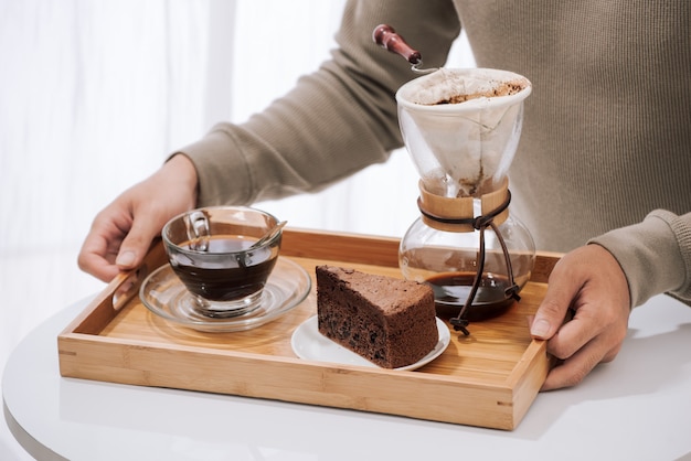 Kaffee auf Holztablett mit Schokoladenkuchen tropfen. Kaffeezeit im Café mit natürlichem Licht