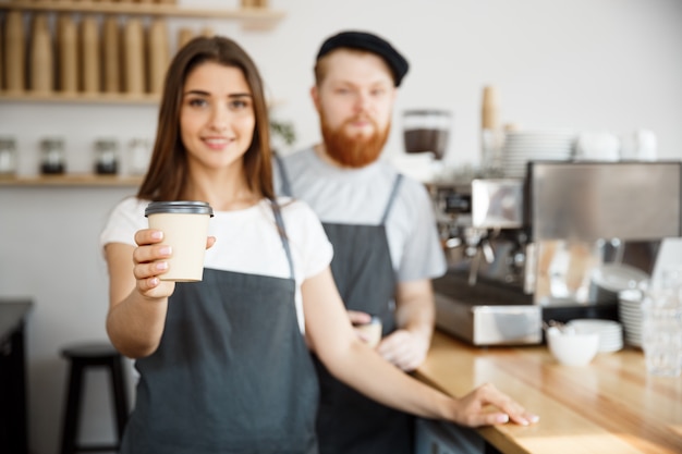 Kaffee Business Concept - Positive junge bärtige Mann und schöne attraktive Dame barista Paar geben mitnehmen Tasse Kaffee zu custome in der modernen Café-Shop