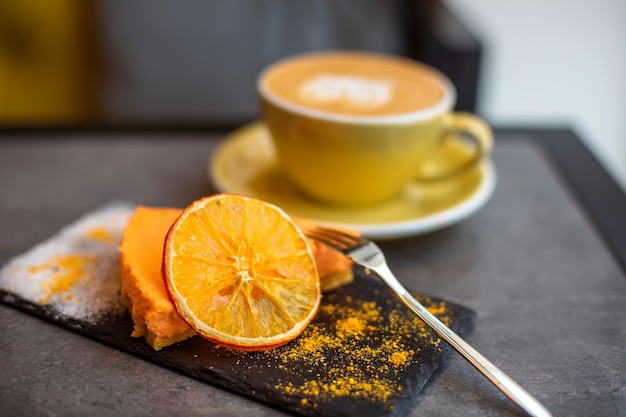 Foto kaffee-cappuccino in gelber tasse mit käsekuchen im café