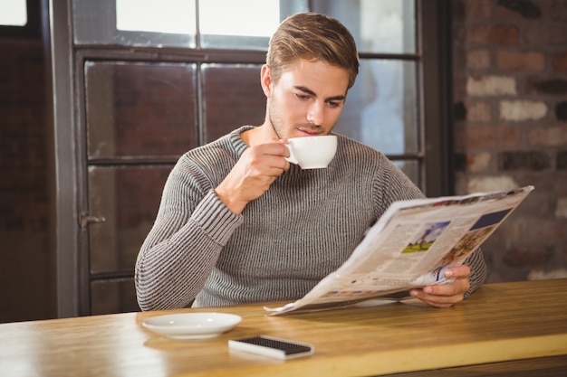 Kaffee des gutaussehenden Mannes trinkend und Zeitung lesend