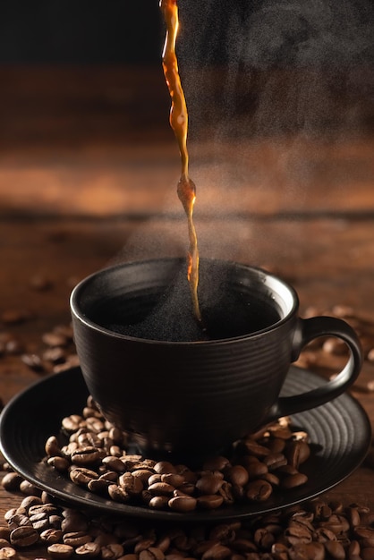 Kaffee heiß und schwarze Tasse, die Kaffee in eine schwarze Tasse auf selektivem Fokus des Fotos im dunklen Lebensmittelstil aus Holz gießt