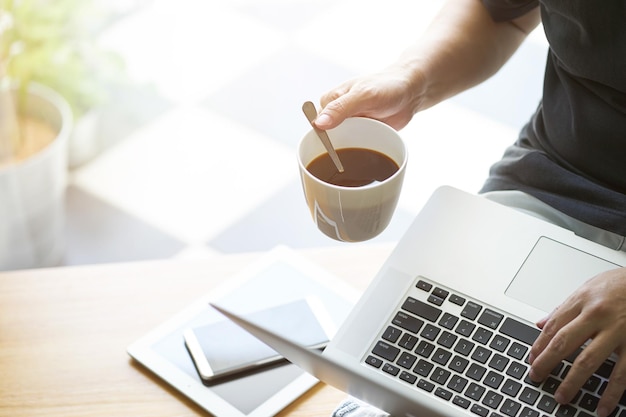 Kaffee in der Hand des Geschäftsmannes mit Laptop, digitalem Tablet, Smartphone und Kaffee