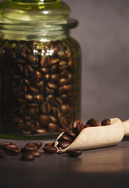 Kaffee in einem Glasgefäß auf einem rustikalen Tisch Kaffeebohnen mit selektivem Fokus in einem Holzlöffel-Porträtbild