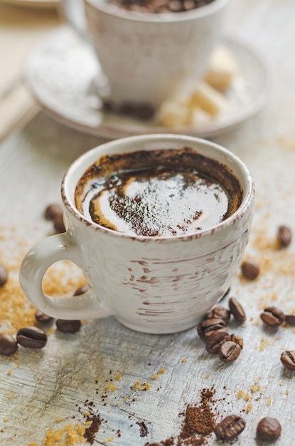 Kaffee in einer kleinen Tasse mit braunem Zuckerrohr und Würfelzucker auf grauem Holztisch