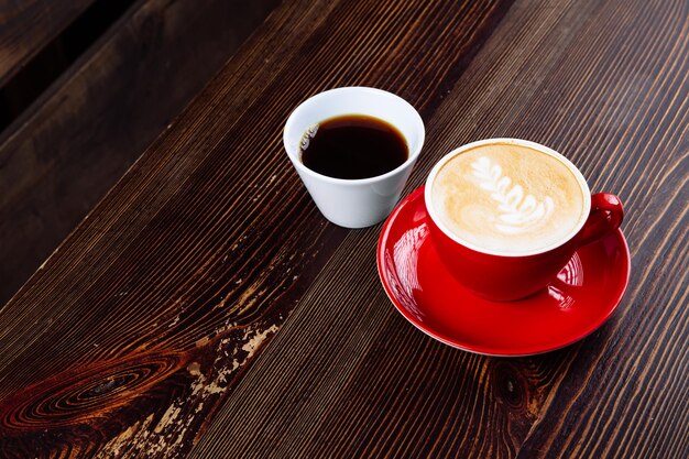 Kaffee in einer roten Tasse mit Milch und Latte Art und Kaffee in einer weißen Tasse auf einem Tisch