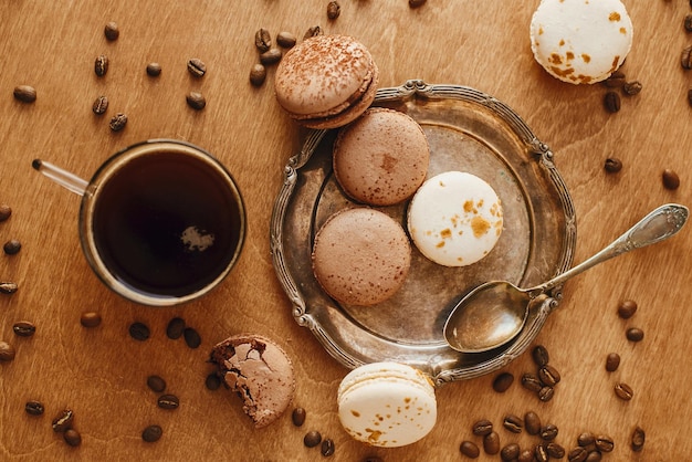 Foto kaffee in glastasse und köstliche makronenkekse auf vintage-platte auf holztisch mit gerösteten kaffeebohnen flach liegend kaffee am morgen und frühstück espresso mit süßigkeiten