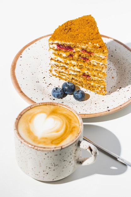 Kaffee, Löffel, Blaubeere, ein Stück Kuchen auf dem Teller auf weißem Hintergrund.