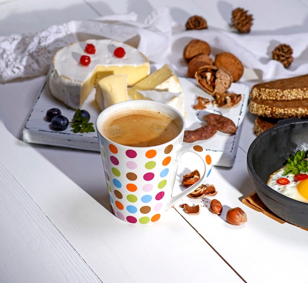 Kaffee mit braunem Schaum in einem weißen Keramikbecher, hinter einem runden Camembert