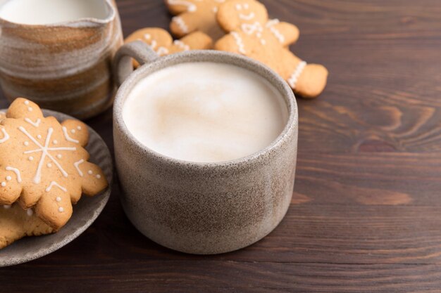 Kaffee mit Milch- und Lebkuchenplätzchen auf hölzernem Hintergrund. Heiße Wintergetränke.